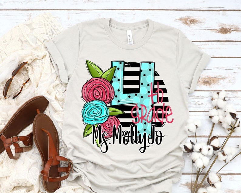 May include: A light gray t-shirt with a black and white striped background. The number 4 is in a blue circle with white polka dots. The text "4th Grade" is written in black. The text "Ms. Molly Jo" is written in black below the number 4. There are pink and blue flowers on the left side of the number 4.