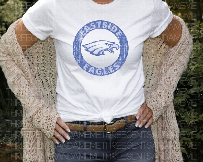 K&ouml;nnte beinhalten: Ein wei&szlig;es T-Shirt mit einem blauen, abgenutzten Kreis-Motiv, auf dem "Eastside Eagles" steht und ein blauer Adler im Kreis zu sehen ist.