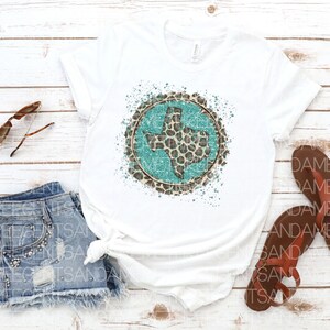 May include: White t-shirt with a turquoise Texas state outline inside a circle of brown leopard print with white paint splatters.