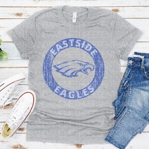 K&ouml;nnte beinhalten: Ein graues T-Shirt mit einem blauen und wei&szlig;en, abgenutzten Kreis-Motiv, auf dem "Eastside Eagles" steht.