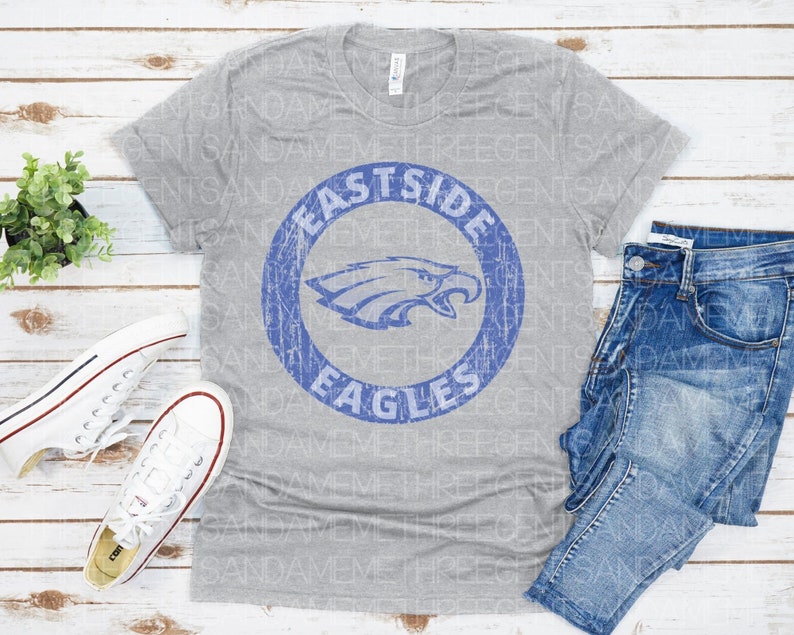 K&ouml;nnte beinhalten: Ein graues T-Shirt mit einem blauen und wei&szlig;en, abgenutzten Kreis-Motiv, auf dem "Eastside Eagles" steht.