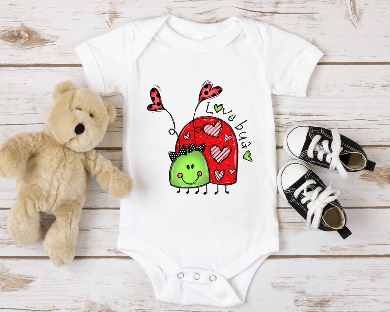 K&ouml;nnte beinhalten: Wei&szlig;er Baby-Strampler mit einem roten und gr&uuml;nen Marienk&auml;fer-Design. Der Marienk&auml;fer hat Herzen auf dem R&uuml;cken und der Text "Love bug" steht daneben.