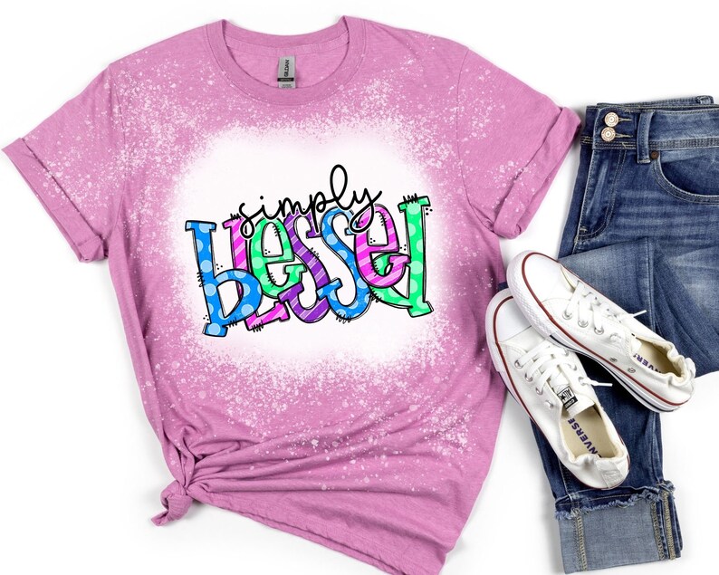 May include: A pink t-shirt with a bleach-splattered design featuring the text "simply blessed" in colorful letters with polka dots.
