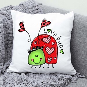 K&ouml;nnte beinhalten: Ein wei&szlig;es Kissen mit einem roten und gr&uuml;nen Marienk&auml;fer-Design. Der Marienk&auml;fer hat schwarze Augen und eine schwarze Schleife. Der Text "Love Bug" ist in gr&uuml;nen Buchstaben auf dem Kissen geschrieben.