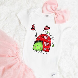 K&ouml;nnte beinhalten: Wei&szlig;er Strampler mit einem roten und gr&uuml;nen Marienk&auml;fer-Design. Der Marienk&auml;fer hat Herzen auf dem R&uuml;cken und der Text "Love Bug" steht an der Seite.