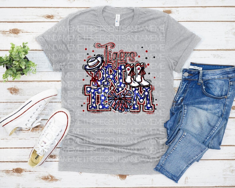 May include: Grey t-shirt featuring a red, white and blue graphic that reads "Tigers Drill Team". The graphic includes a cheerleader, pom-poms and a hat.