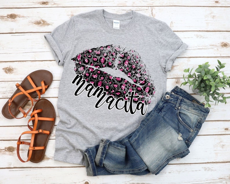 Pu&ograve; includere: Una maglietta grigia con un design a labbra con stampa leopardata rosa e nera e la parola "mamacita" in testo nero.