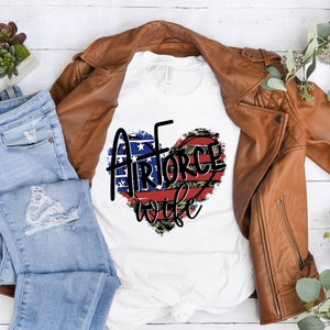 May include: White t-shirt with a red, white, and blue heart design with the words "Air Force Wife" in black text.