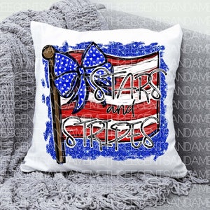 May include: A white pillow with a red, white, and blue American flag design. The flag has a blue bow with white stars on it. The text "Stars and Stripes" is written in black letters on the flag.