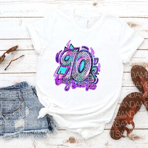 Pode incluir: Camiseta branca com um design gr&aacute;fico do n&uacute;mero 90 em um padr&atilde;o colorido, brilhante e xadrez. O texto "Bring it on the 90's" est&aacute; escrito em uma fonte roxa neon.