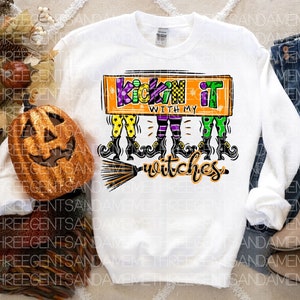 May include: White long-sleeved sweatshirt with a graphic of three witches with broomsticks and the text "Kickin' it with my witches".