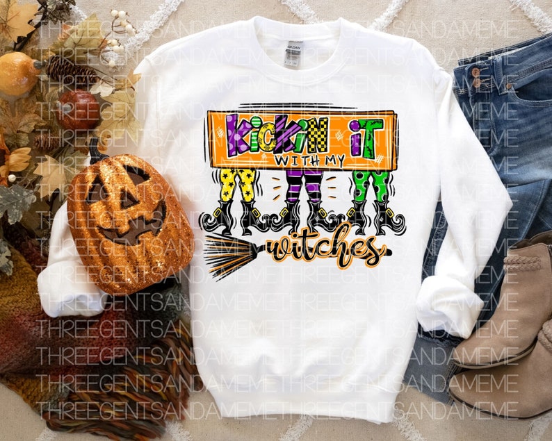May include: White long-sleeved sweatshirt with a graphic of three witches with broomsticks and the text "Kickin' it with my witches".
