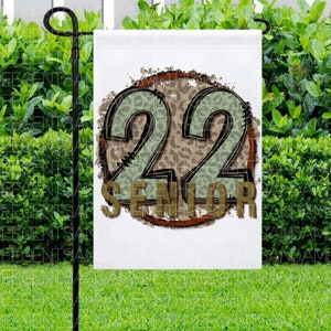 Puede incluir: Una bandera de jard&iacute;n blanca con un c&iacute;rculo marr&oacute;n y el n&uacute;mero 22 en verde y marr&oacute;n con un estampado de leopardo. El texto "Senior" est&aacute; debajo del n&uacute;mero 22.