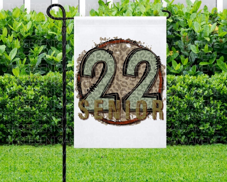 Puede incluir: Una bandera de jard&iacute;n blanca con un c&iacute;rculo marr&oacute;n y el n&uacute;mero 22 en verde y marr&oacute;n con un estampado de leopardo. El texto "Senior" est&aacute; debajo del n&uacute;mero 22.