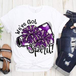 Op de afbeelding: Wit T-shirt met een afbeelding van een paarse en witte glitterpompon en een megafoon. De tekst "We've Got Spirit!" is op het shirt gedrukt.