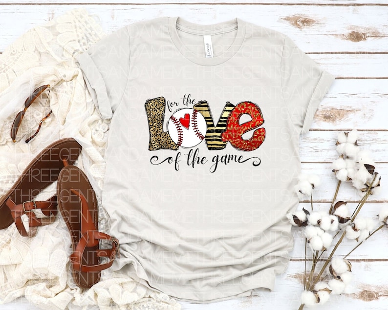 May include: A white t-shirt with a graphic design of the word "LOVE" with a baseball in the center. The letters are decorated with leopard print, stripes, and red glitter. The text "for the love of the game" is written below the graphic.