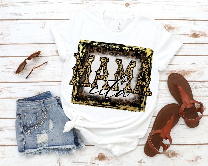 May include: White t-shirt with a gold and black distressed frame featuring a leopard print design and the text "Mamacita".