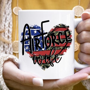 May include: White ceramic mug with a red, white, and blue heart design. The heart has a distressed look and the text "Airforce wife" is written in black.