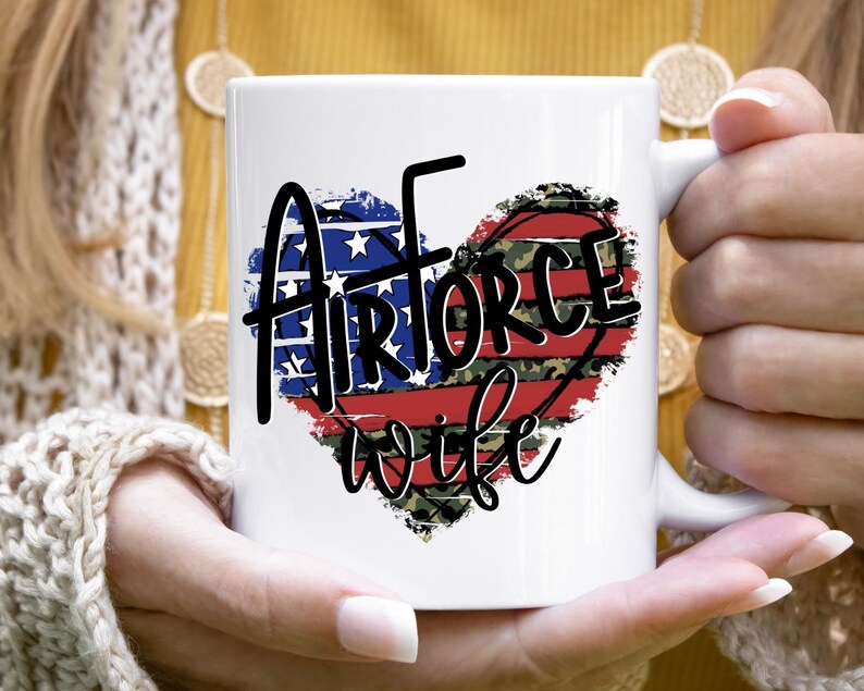 May include: White ceramic mug with a red, white, and blue heart design. The heart has a distressed look and the text "Airforce wife" is written in black.