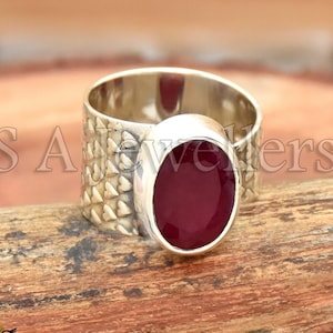 May include: A silver ring with a textured band and a large oval-shaped ruby gemstone.