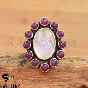 May include: A silver ring with a large oval moonstone surrounded by a halo of small, deep pink gemstones.