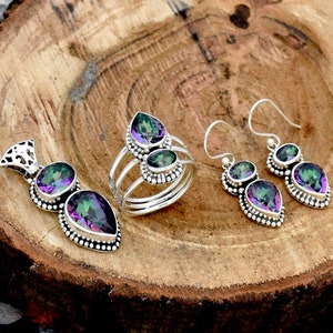 May include: A set of three silver rings featuring iridescent gemstones. Each ring has a teardrop design with three stones, showcasing a blend of green, purple and blue hues.