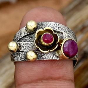 Op de afbeelding: Een zilveren en gouden ring met drie rode robijnstenen. De ring heeft een getextureerde band en een bloemmotief met een robijn in het midden.
