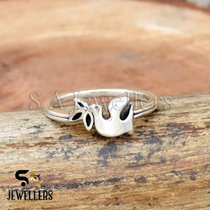 Op de afbeelding: Een zilveren ring met een duif en olijftak ontwerp. De ring ligt op een houten oppervlak.