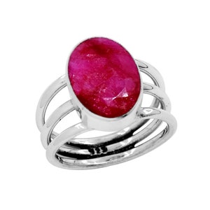 Może przedstawiać: Srebrny pierścionek z dużym, owalnym rubinem. Jasnoczerwony rubin osadzony jest w oprawie typu bezel i otoczony potrójnym paskiem. Pierścionek to efektowny element, który podkreśla kolor i blask kamienia szlachetnego.
