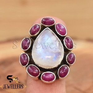 May include: A silver ring with a large pear-shaped moonstone and a halo of smaller pink gemstones.