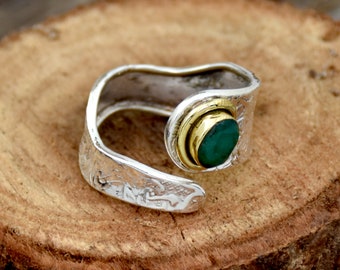 May include: A silver ring with a green gemstone set in a gold bezel. The ring is textured and has a unique design.