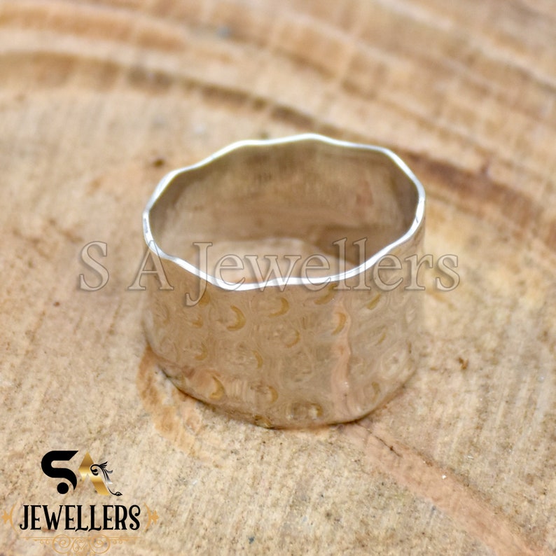 May include: A silver ring with a textured surface and a hammered design. The ring is wide and has a rounded shape.