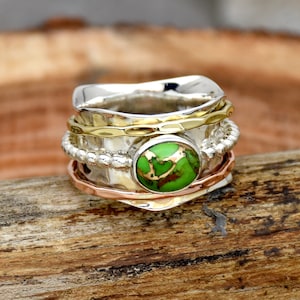 May include: A silver, gold, and copper ring with a green turquoise stone. The ring is made of multiple bands and has a hammered texture.