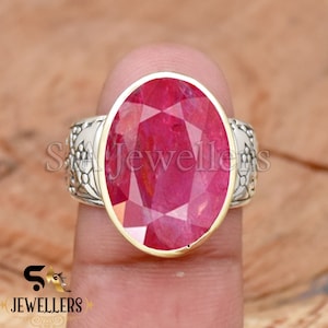 Può includere: Un anello d'argento con una pietra preziosa rossa di forma ovale incastonata in una ghiera d'oro. L'anello ha un design floreale dettagliato sulla fascia.