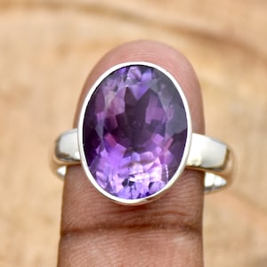 Könnte beinhalten: Ein silberner Ring mit einem großen ovalen Amethyst-Edelstein. Der Amethyst ist tiefviolett und hat einen facettierten Schliff.