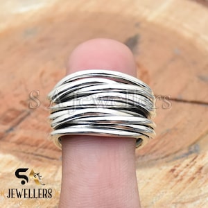 Può includere: Un anello d'argento fatto di più bande sottili intrecciate. L'anello è indossato su un dito.