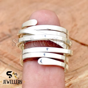May include: A silver ring with multiple bands that are twisted and intertwined. The ring is worn on a finger.