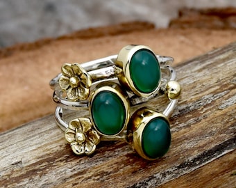 May include: Three silver rings with green gemstones and gold accents. The rings are stacked on top of each other and feature small flower designs.