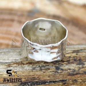 May include: A silver hammered band ring with a textured surface. The ring is thick and wide.