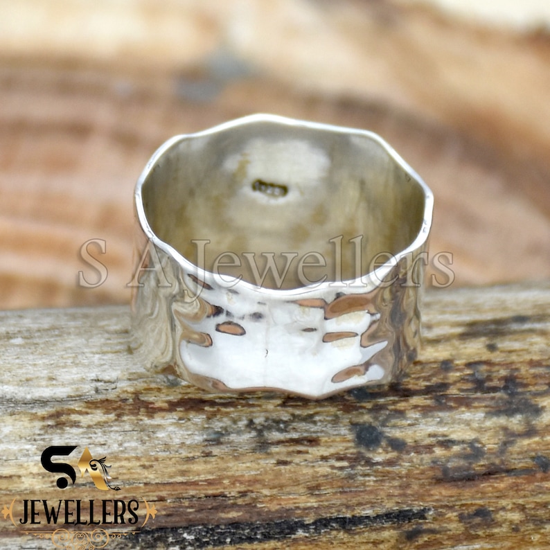 May include: A silver hammered band ring with a textured surface. The ring is thick and wide.