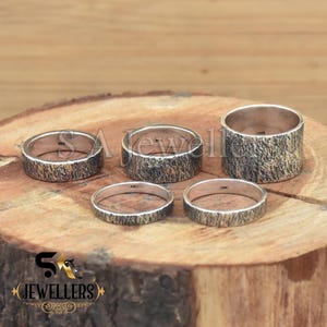 K&ouml;nnte beinhalten: Vier silberne Ringe mit einer strukturierten Oberfl&auml;che. Die Ringe liegen auf einer Holzoberfl&auml;che.
