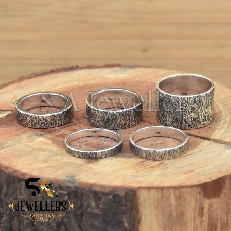 K&ouml;nnte beinhalten: Vier silberne Ringe mit einer strukturierten Oberfl&auml;che. Die Ringe liegen auf einer Holzoberfl&auml;che.