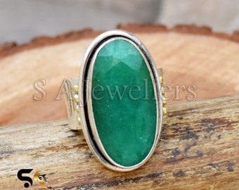 May include: A silver ring with a large oval green gemstone set in a silver bezel. The ring is accented with small gold beads around the bezel.