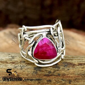 May include: A silver ring with a pink gemstone set in a triangular shape. The ring is made of twisted silver wire and has a unique design.