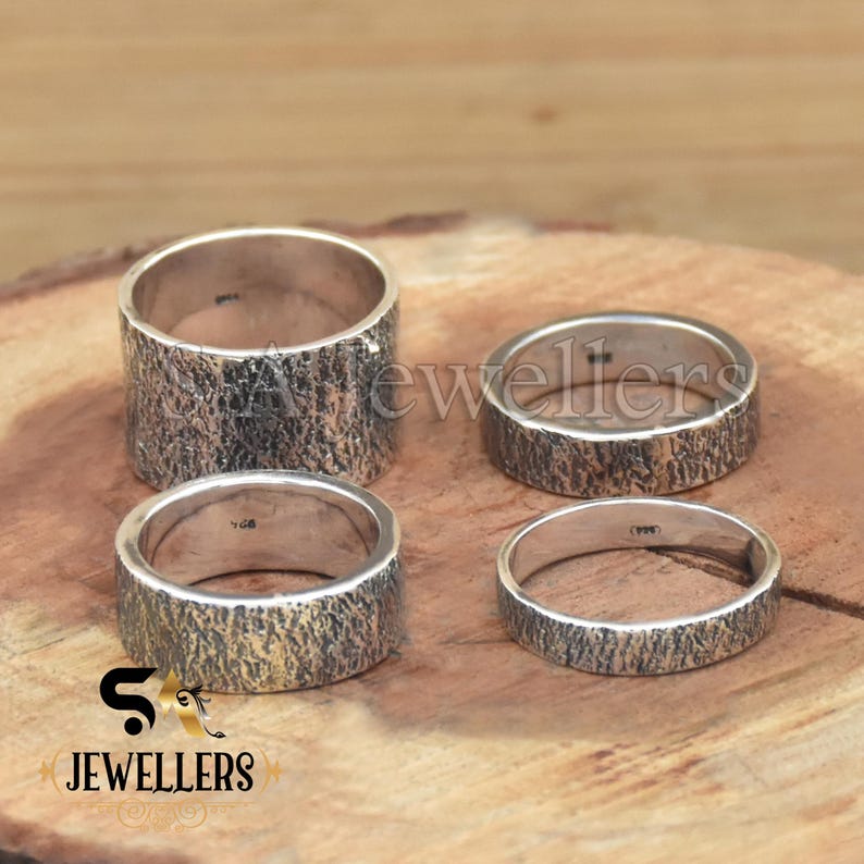 K&ouml;nnte beinhalten: Vier silberne Ringe mit einer strukturierten, holz&auml;hnlichen Oberfl&auml;che. Die Ringe liegen auf einer Holzoberfl&auml;che.