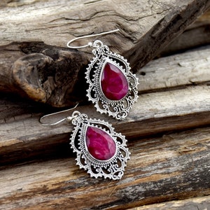 May include: A pair of silver filigree earrings with teardrop-shaped pink ruby gemstones.