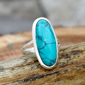 May include: A silver ring with a large oval turquoise gemstone. The turquoise is a vibrant blue-green color with dark veins running through it.