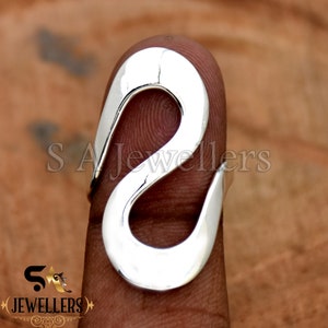 May include: A silver ring with a unique, abstract design. The ring is shaped like a stylized letter 'S' with a smooth, polished finish.