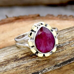 May include: A pear-shaped ruby gemstone ring with a gold setting and a silver band.