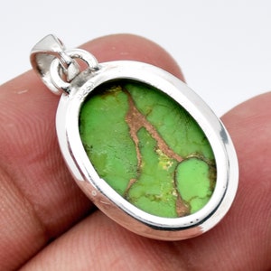 May include: Oval shaped pendant with a green turquoise stone set in sterling silver. The stone has copper veins running through it.